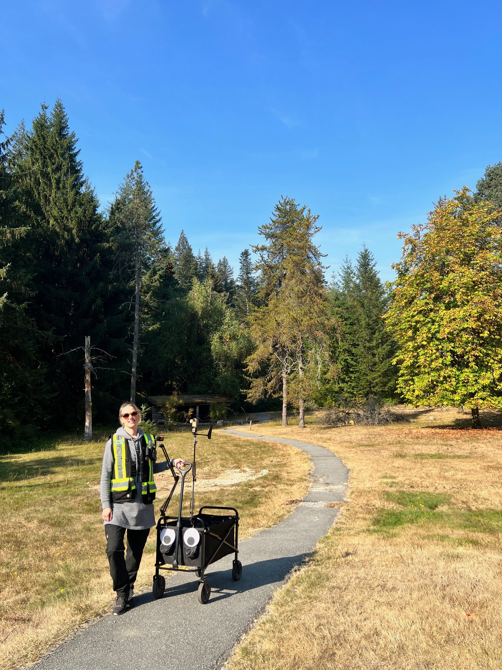 Tara Tiger Brown walking a paved trail with a field cart of acoustic and microclimate sensors